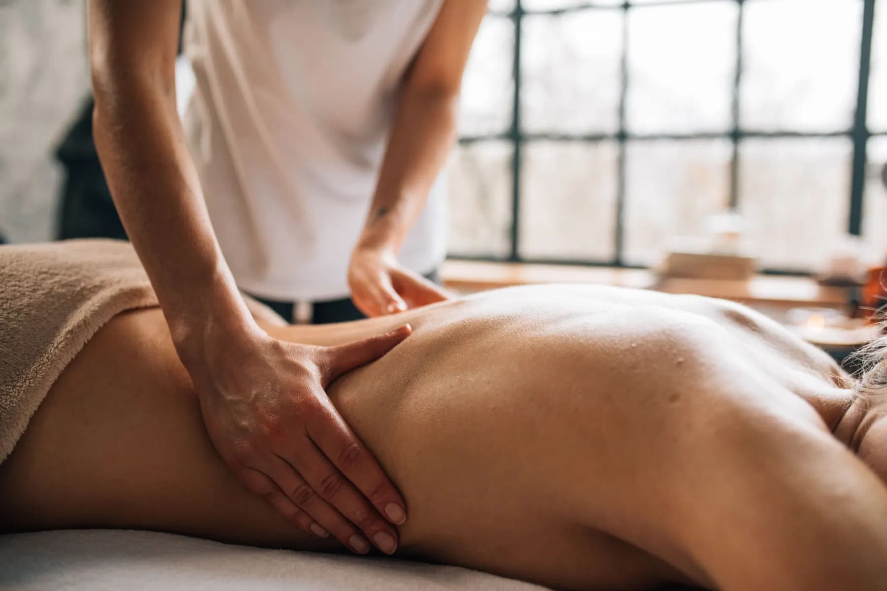 Back work on a massage table beside a tall loft window